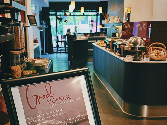 The hotel’s breakfast area, featuring a buffet, warm lighting and a sign reading ‘Good Morning’ in the foreground.