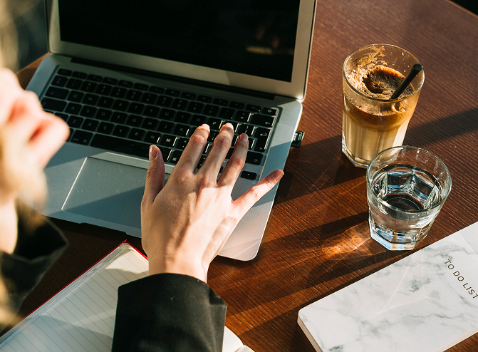 A person is working on a laptop with a coffee and a glass of water beside them.