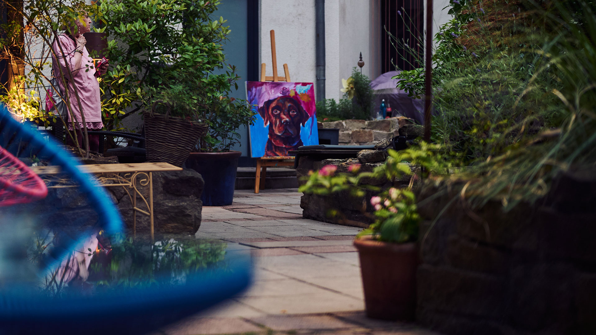 Hidden city garden with lush plants, seating areas, and a colourful dog portrait on an easel.