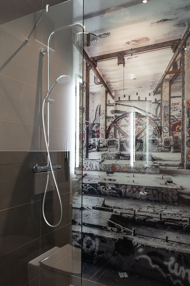 Modern bathroom with a glass shower and an urban Ruhrpott-style wall design.