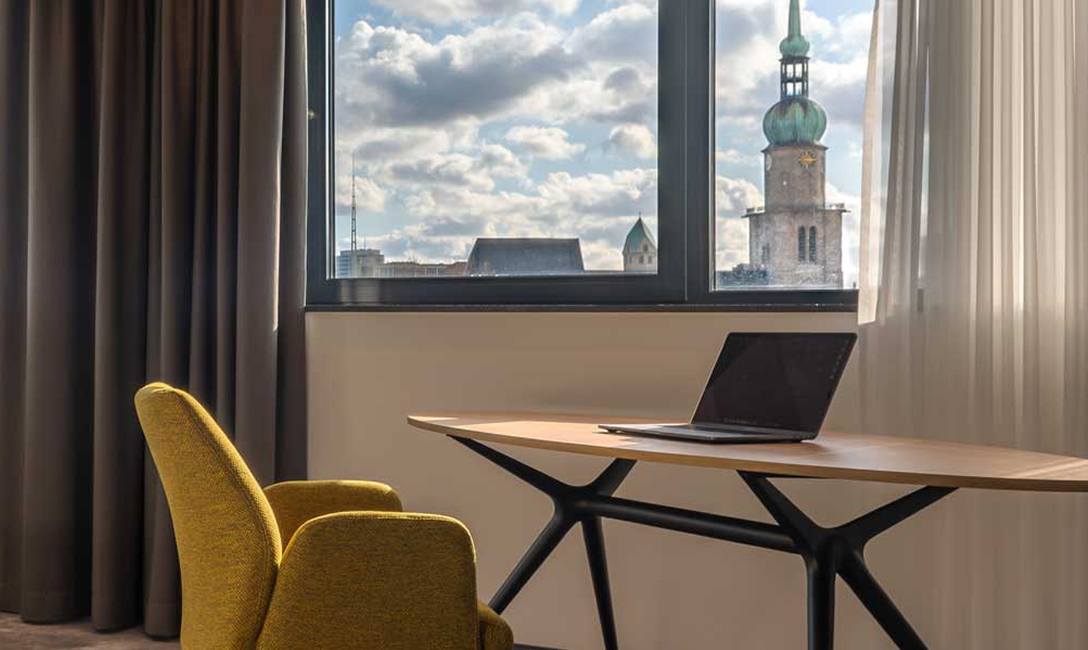 Hotel room with a desk, laptop, and a view of Dortmund city centre.